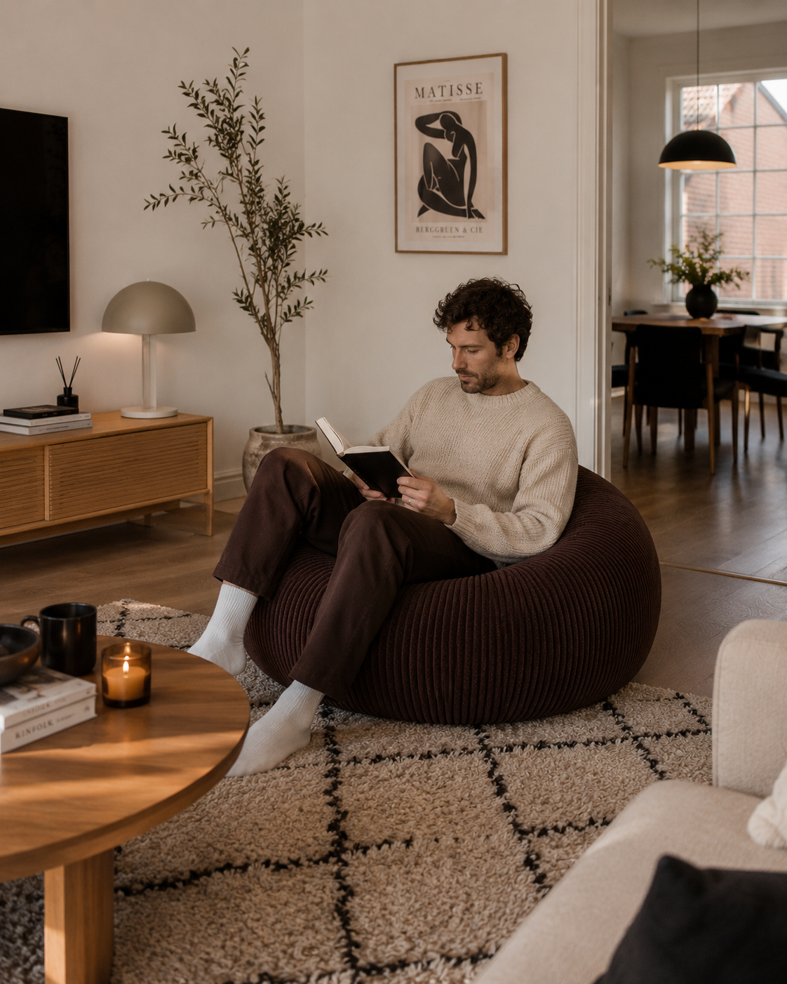 Homme lisant dans un pouf côtelé moka Mowana dans un salon moderne et chaleureux à l’ambiance cocooning