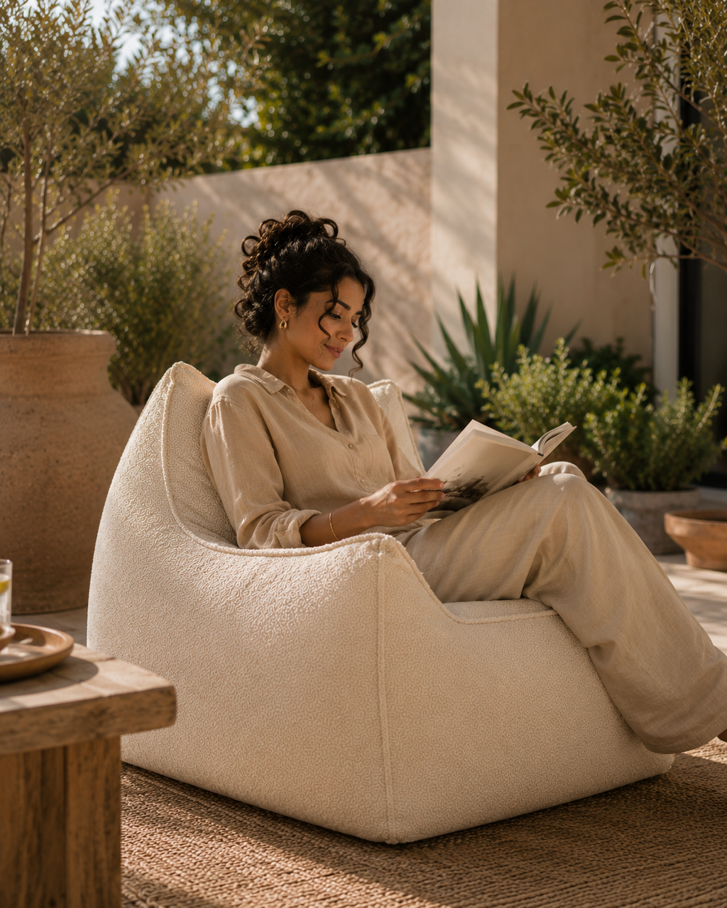 Femme lisant sur un pouf fauteuil carré velours blanc Mowana en extérieur dans une ambiance méditerranéenne chaleureuse